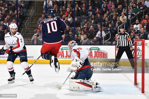 Alexander Wennberg of the Columbus Blue Jackets jumps to avoid the puck as it goes past goaltender Braden Holtby of the Washington Capitals during...