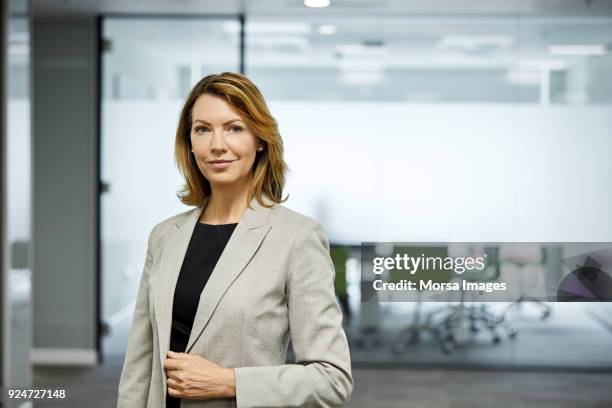 mature businesswoman standing against board room - fato imagens e fotografias de stock