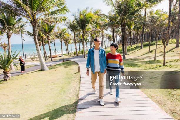 happy mature couple enjoying vacation by the seaside - asian couple walking stock pictures, royalty-free photos & images