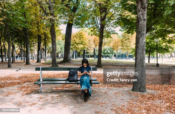 young woman using smartphone in a park - women smartphone city paris stock pictures, royalty-free photos & images