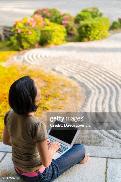 zijaanzicht van de vrouw zitten op het podium van de tempel, typen op een laptop terwijl u geniet van zen tuin van chion-ji tempel in kyoto, japan - kumikomini stockfoto's en -beelden