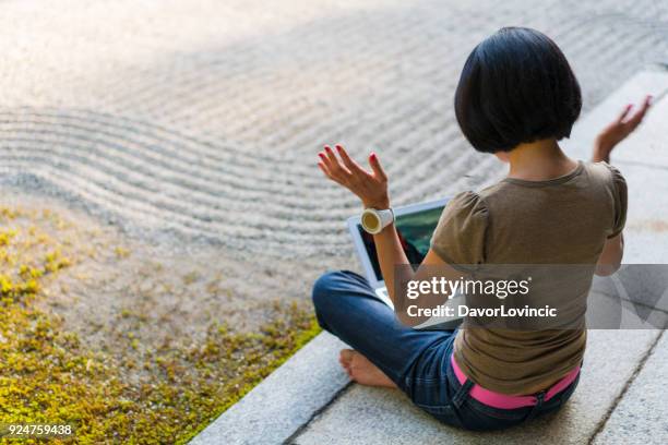 seite, rückansicht frau auf tempel podium sitzen, mit blick auf einen laptop, verbreitung von händen und genießen sie zen-garten von chion-ji-tempel in kyoto, japan - kumikomini stock-fotos und bilder