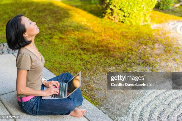 seitenansicht der frau sitzt auf tempel podium, denken mit erhobenem kopf beim tippen auf einen laptop und genießen zen-garten von chion-ji-tempel in kyoto, japan - kumikomini stock-fotos und bilder