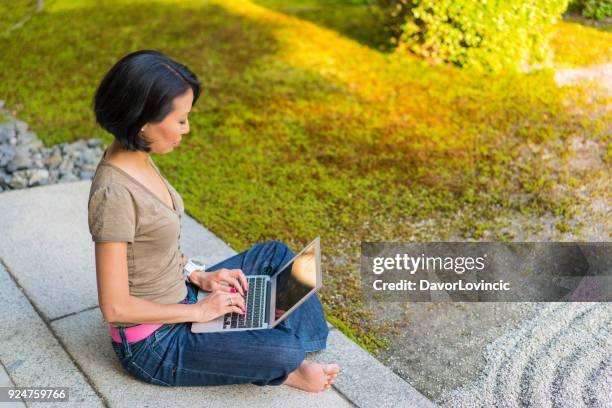 zijaanzicht van de vrouw zitten op het podium van de tempel, typen op een laptop terwijl u geniet van zen tuin van chion-ji tempel in kyoto, japan - kumikomini stockfoto's en -beelden