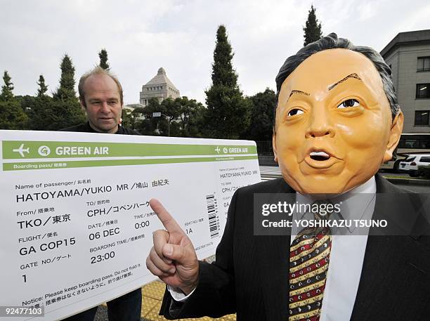 Member of environmental group Greenpeace, wearing a mask of Japanese Prime Minister Yukio Hatoyama , points to a large mock-up air ticket to...