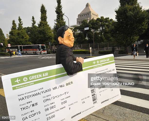 Member of environmental group Greenpeace, wearing a mask of Japanese Prime Minister Yukio Hatoyama, carries a large mock-up air ticket to Copenhagen...