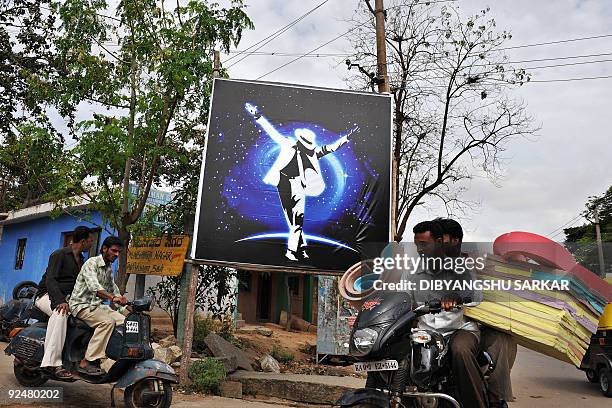 Indian commuters ride past a poster of late US performer Michael Jackon, erected by local fans, in Bangalore on October 29, 2009. Michael Jackson has...