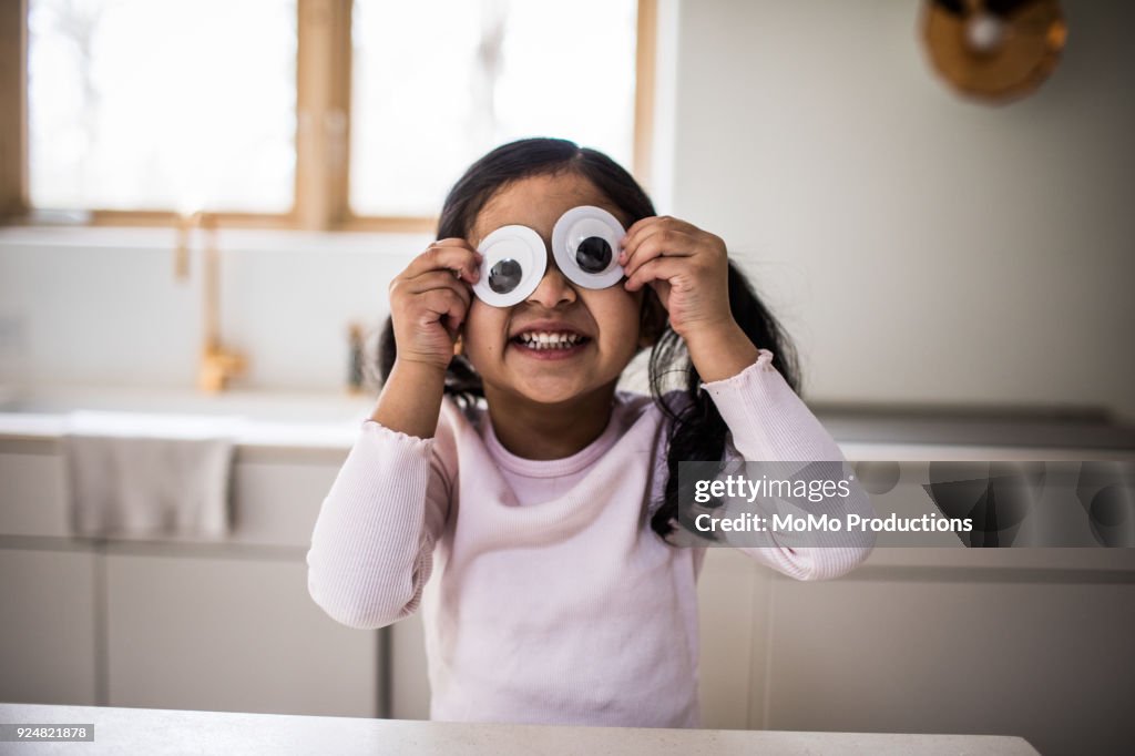 Young girl playing with silly googly eyes at home