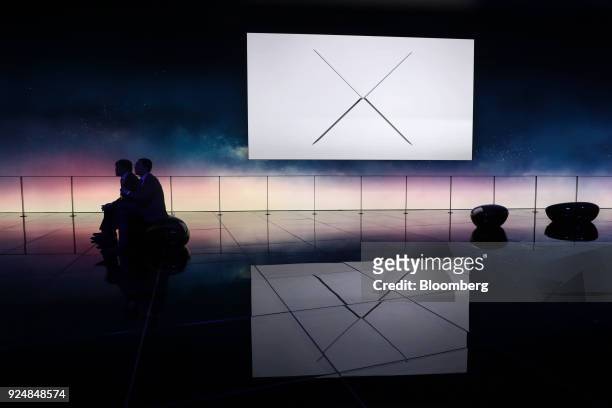 Attendees sit as an electronic screen displays images of the MateBook X Pro laptop computer at the Huawei Technologies Co. Pavilion during day two of...