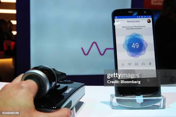 An attendee uses a Vital Moto Mod modular health monitoring system to check pulse rate on the Lenovo Group Ltd. Stand during day two of the Mobile...