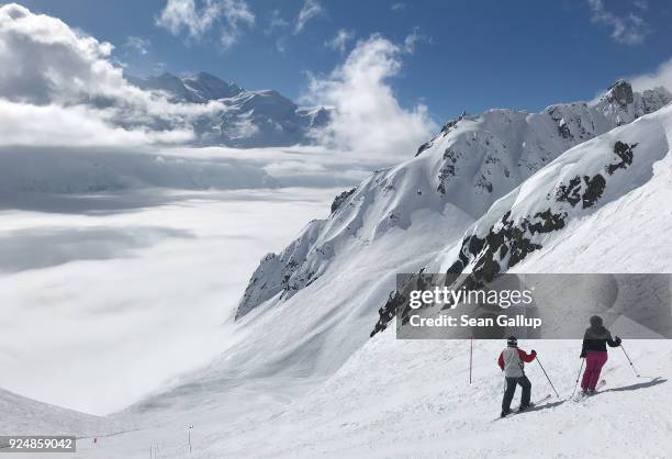Alpine skiers prepare to ski down a piste into clouds at La Flegere ski resort as the Mont Blanc summit is seen in the distance on February 25, 2018...