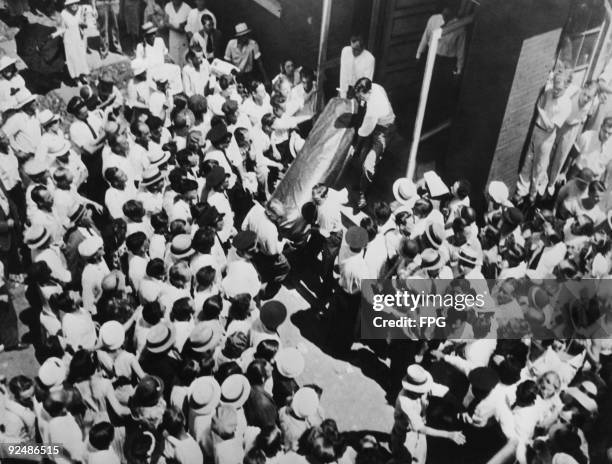 The body of American bank robber John Dillinger is brought out of a Chicago funeral home, watched by a crowd of onlookers, 24th July 1934. It will be...