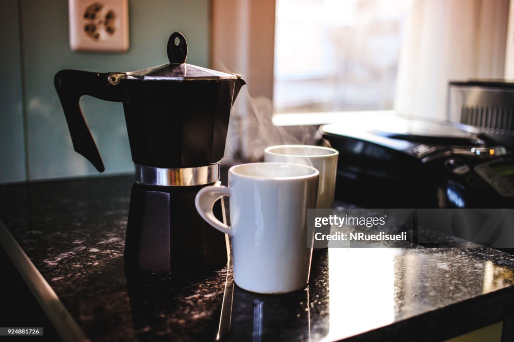在電爐上莫卡鍋裡準備新鮮咖啡。把熱蒸咖啡倒入兩個白色杯子裡。