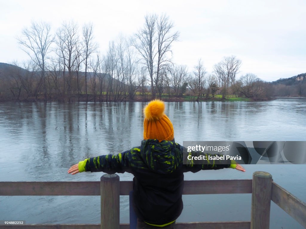 Rear View Of Child On Bridge By Lake During Winter