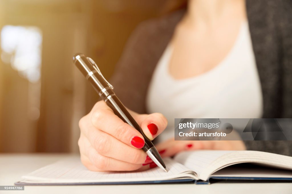 Female hands with pen writing on notebook. Diary, plans, journalist