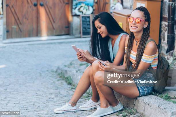 zwei mädchen sitzen auf der straße und mit smartphones - auf dem boden sitzen stock-fotos und bilder