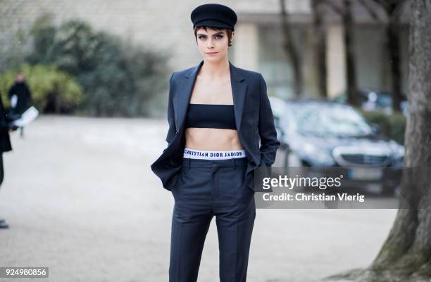 Model Cara Delevingne wearing a cropped top, navy pants, military hat is seen outside Dior on February 27, 2018 in Paris, France.
