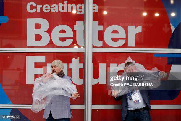 Two attendees use plastic raincoats to protect themselves from the rain outside the Mobile World Congress venue on February 27, 2018 in Barcelona....