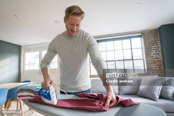 handsome single guy at home ironing his clothes looking happy - ironing stock pictures, royalty-free photos & images