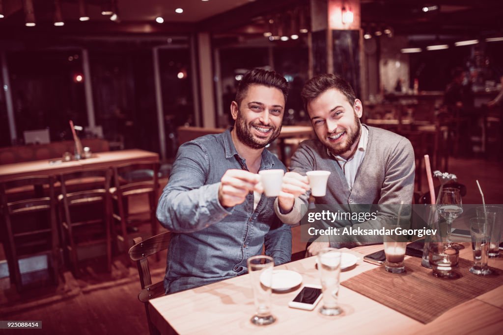 Two Handsome Friends Drink Coffee in a Bar and Toasting to the Camera