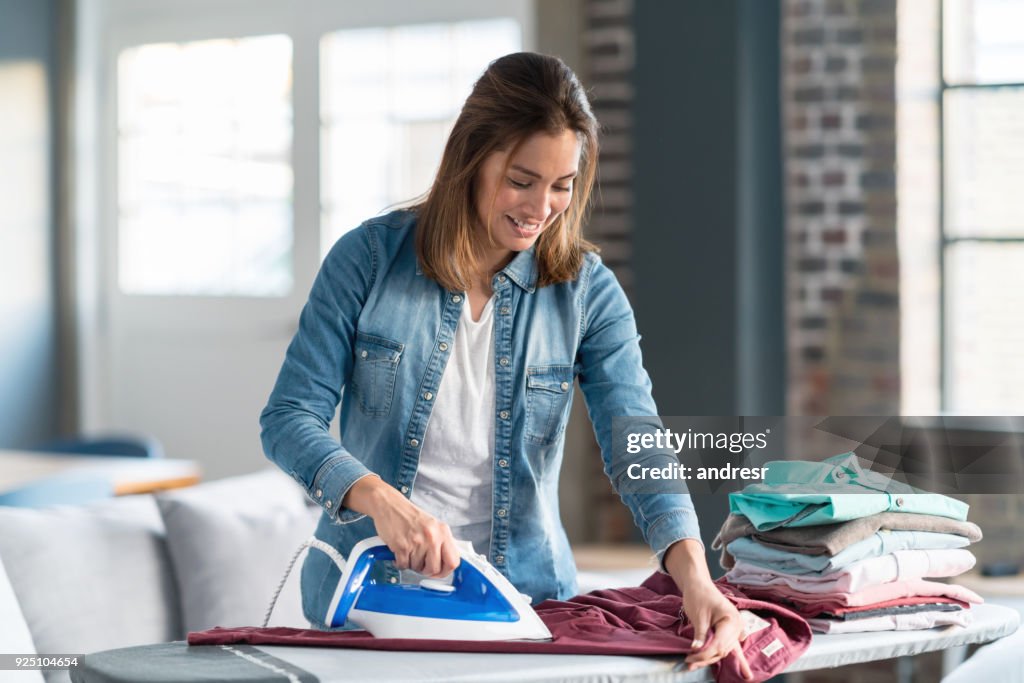 Happy woman ironing her clothes at home