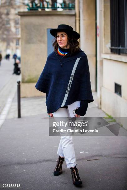 Deborah Reyner Sebag wears white pants, black cloak and black hat in the streets of Paris before the Dior show during Paris Fashion Week Womenswear...