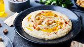 Hummus, chickpea dip, with spices and pita, flat bread in a black plate on grey stone background. Top view.