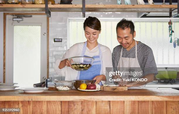 a couple cutting ingredients in the kitchen. - mid adult couple stock pictures, royalty-free photos & images