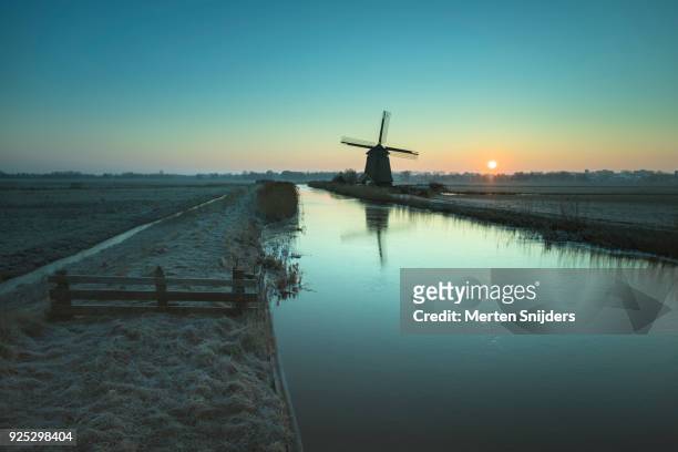 classical dutch windmill amidst frozen countryside - merten snijders stock-fotos und bilder
