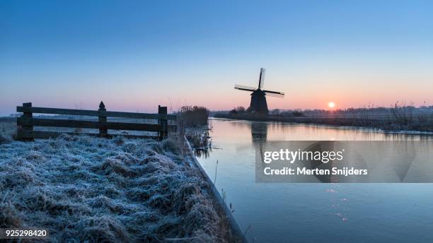 classical dutch windmill amidst frozen countryside - merten snijders stock-fotos und bilder