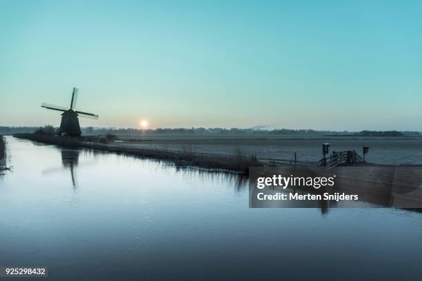 classical dutch windmill amidst frozen countryside - merten snijders stock-fotos und bilder