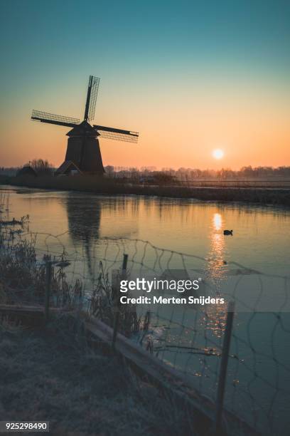 classical dutch windmill amidst frozen countryside - merten snijders stock-fotos und bilder