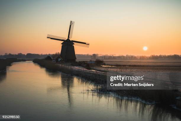 classical dutch windmill amidst frozen countryside - merten snijders stock-fotos und bilder