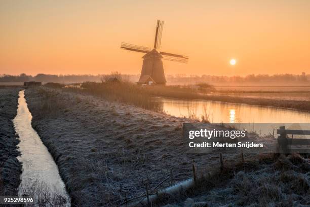 classical dutch windmill amidst frozen countryside - merten snijders stock-fotos und bilder