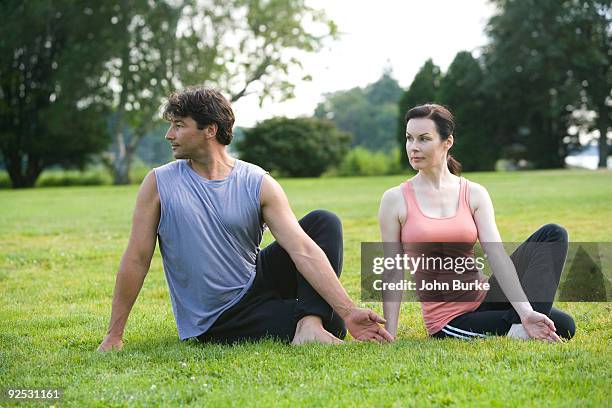 couple doing yoga poses in a park - ardha matsyendrasana stock-fotos und bilder