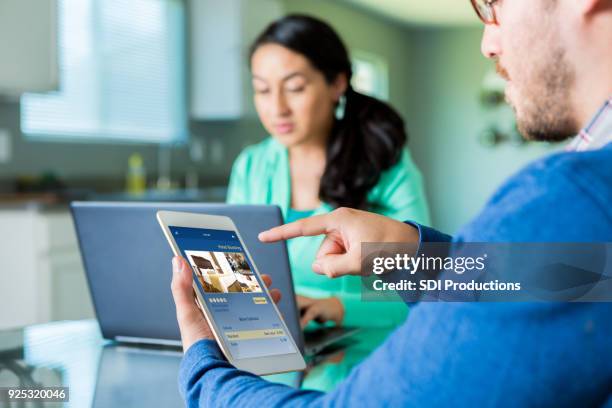 hombre usa su tablet en casa una reserva de hotel - hacer una reserva fotografías e imágenes de stock