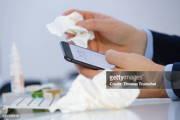 Berlin, Germany Symbolic photo on the topic 'germs on the smartphone'. A person with cold holds a smartphone in one hand, and a handkerchief in the...
