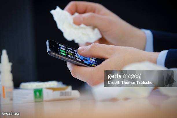 Berlin, Germany Symbolic photo on the topic 'germs on the smartphone'. A person with cold holds a smartphone in one hand, and a handkerchief in the...