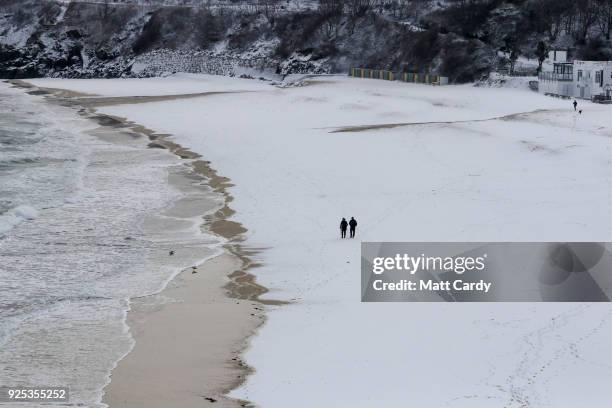 People walk on the snow covering the sand at Carbis Bay as snow arrives in St Ives on February 28, 2018 in Cornwall, England. Freezing weather...