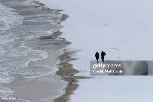 People walk on the snow covering the sand at Carbis Bay as snow arrives in St Ives on February 28, 2018 in Cornwall, England. Freezing weather...