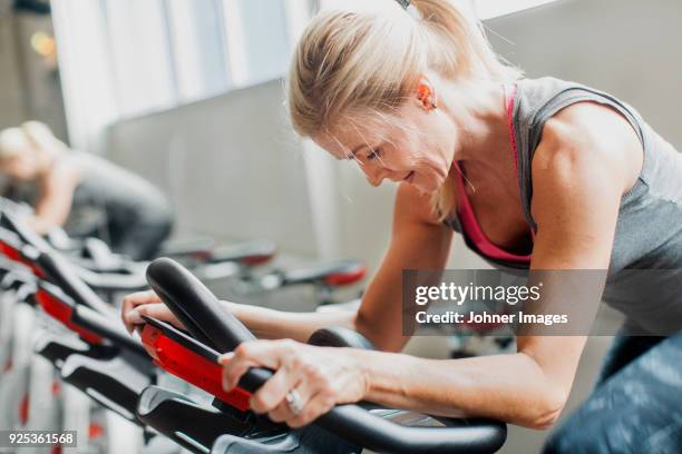 woman exercising on stationary bicycle in gym - spinning stock-fotos und bilder