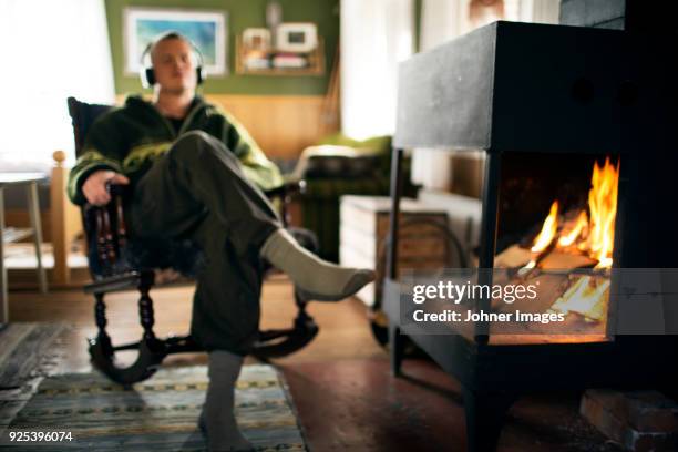 man listening to music next to fireplace - haardvuur stockfoto's en -beelden