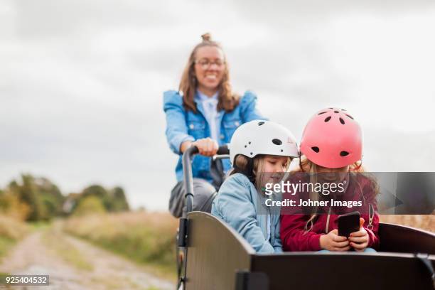 mother pushing daughters in bicycle cart - helmet cart stock pictures, royalty-free photos & images