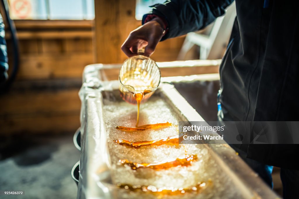 Person pouring maple syrup onto snow at sugar shack
