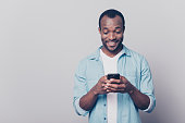 Portrait of handsome excited cheerful joyful delightful curious guy wearing casual jeans denim shirt sending and getting messages to his lover isolated on gray background