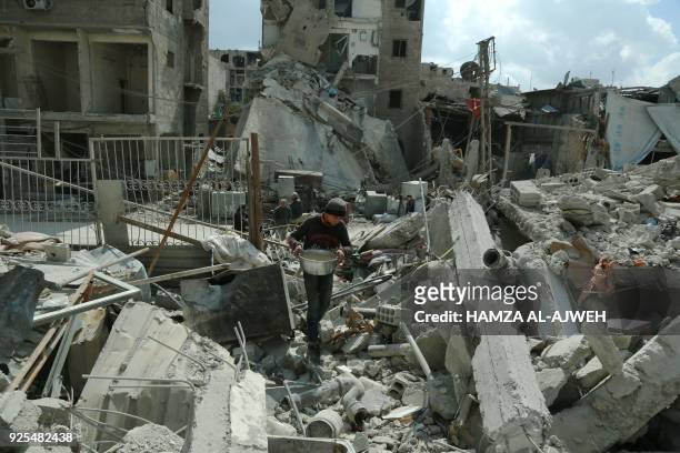 Syrian boy carries food as he walks amid the rubble of buildings which were destroyed earlier in regime air strikes, in the rebel-held besieged town...