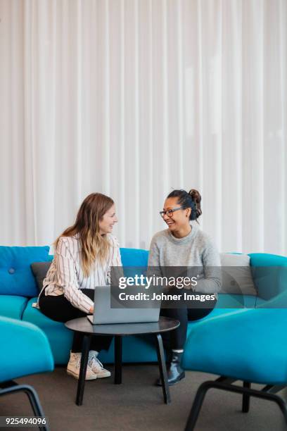 two friends sitting in living room with laptop - friends talking living room stock-fotos und bilder