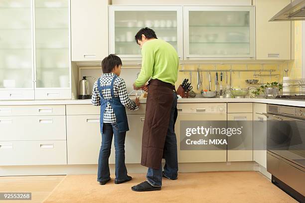 father and son cooking - schürze mann rückansicht stock-fotos und bilder