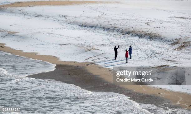 People walk on the snow covering the sand at Carbis Bay as snow arrives in St Ives on February 28, 2018 in Cornwall, England. Freezing weather...