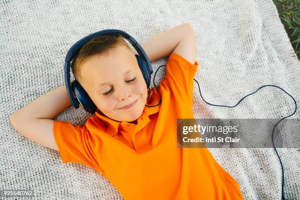 smiling caucasian boy laying on blanket in park listening to headphones - child listening differential focus stock pictures, royalty-free photos & images